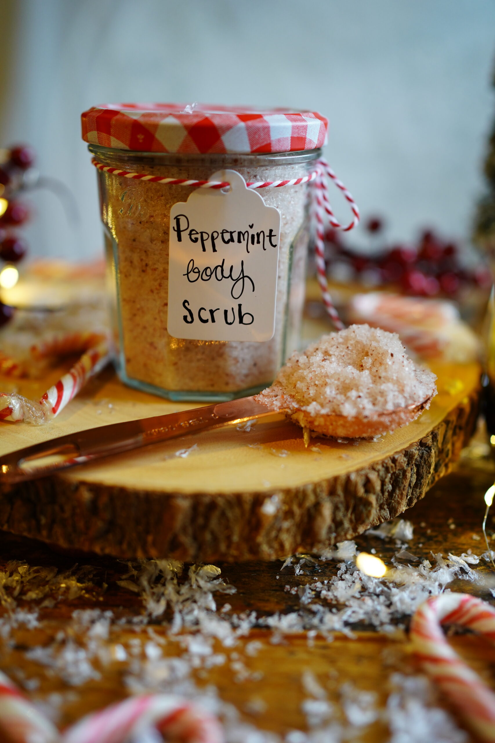 a jar of peppermint body scrub in a glass jar sitting on a wooden slab with a spoon of salt in front