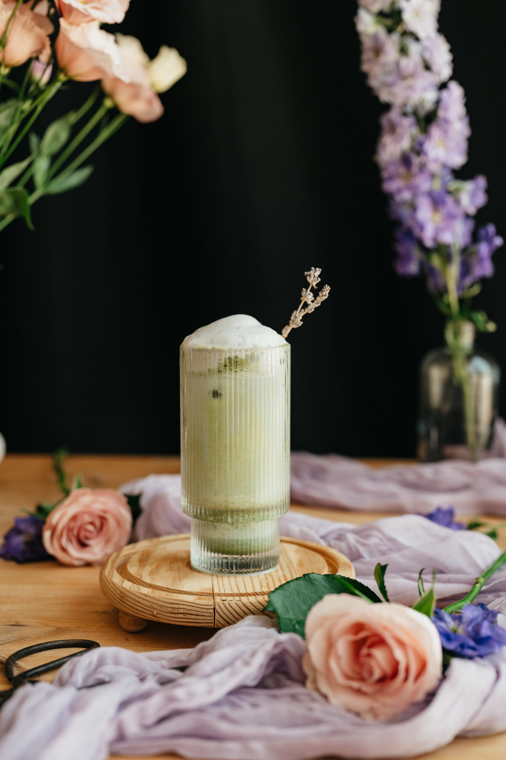 a glass of lavender matcha latte in a glass on a wooden stand