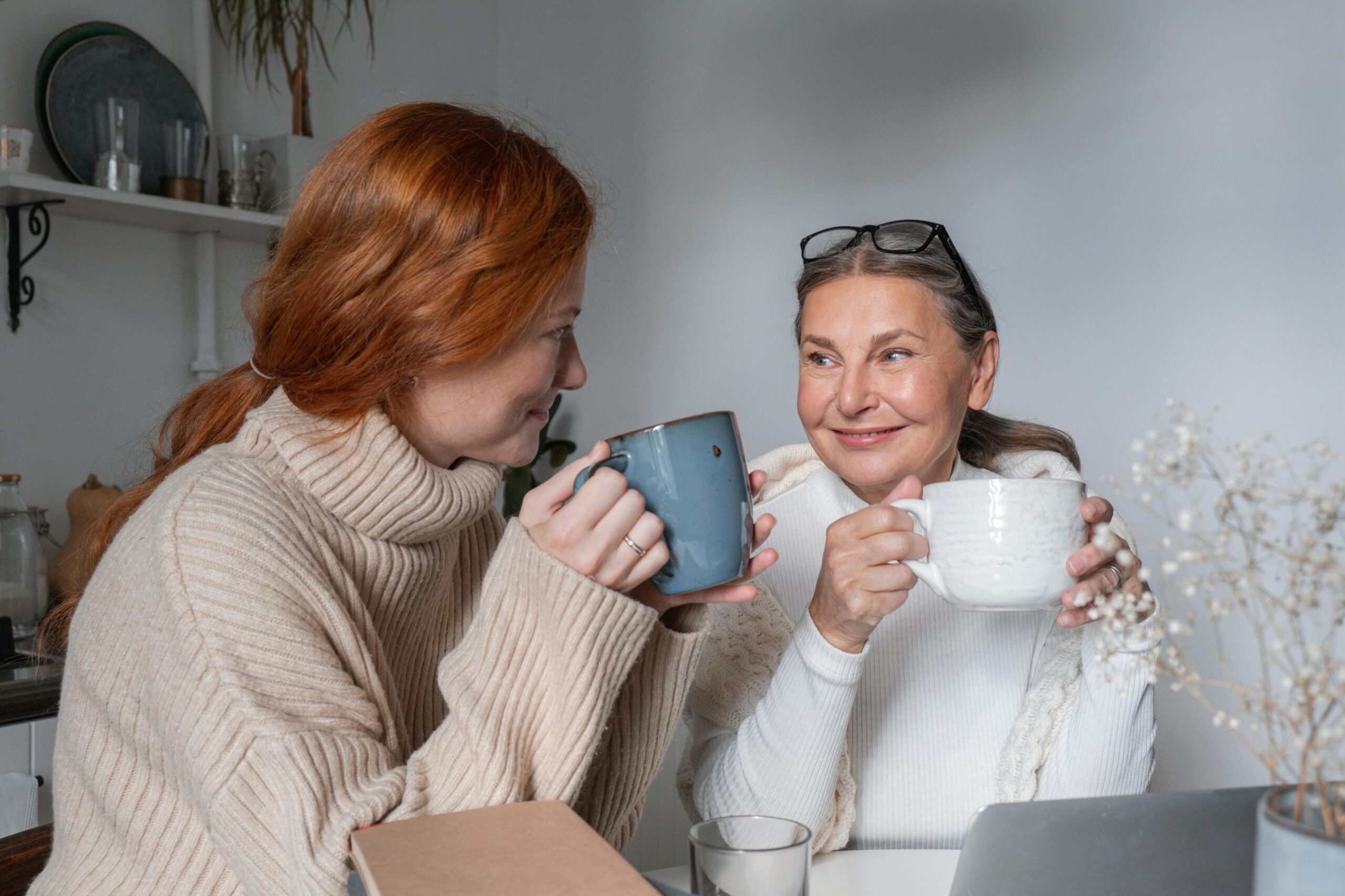 two women looking at each other while drinking from mugs