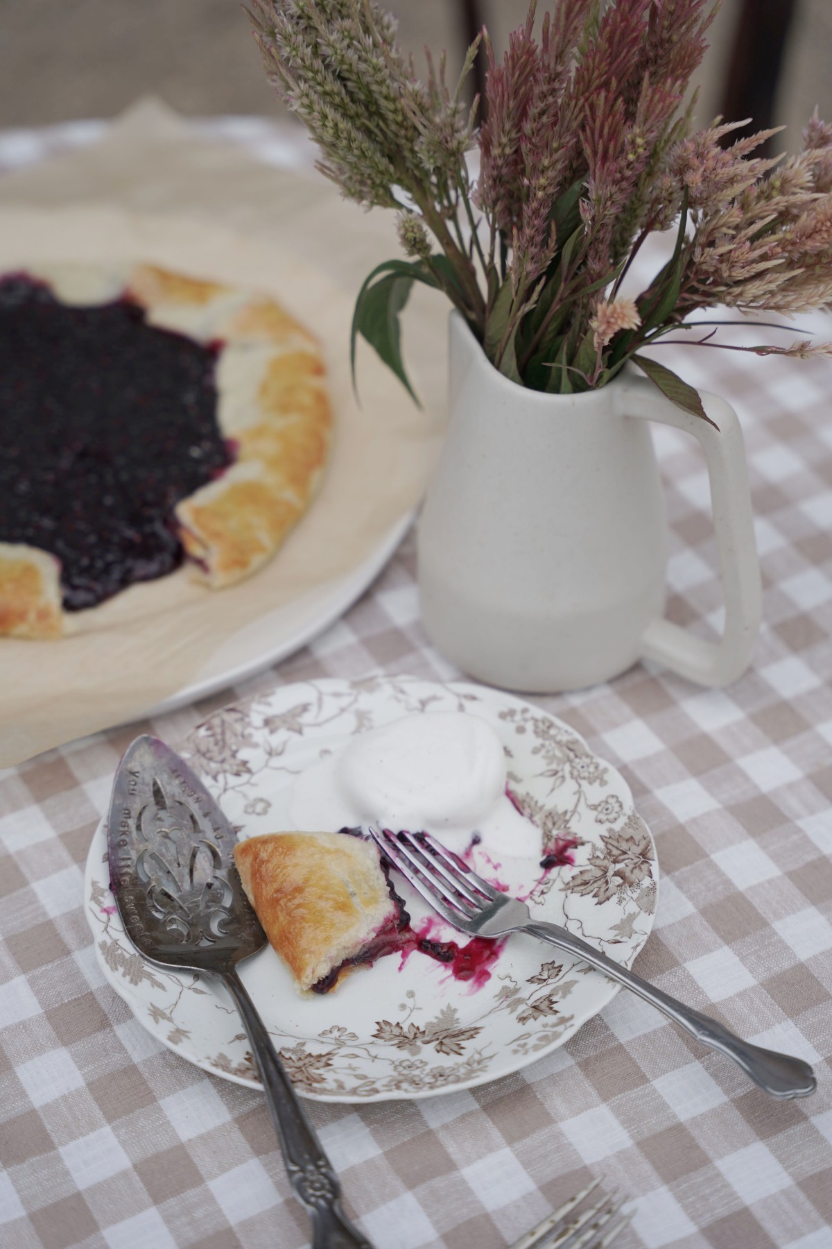 a slice of Elderberry Spice Galette on a plate with ice cream with a platter of galette in the background