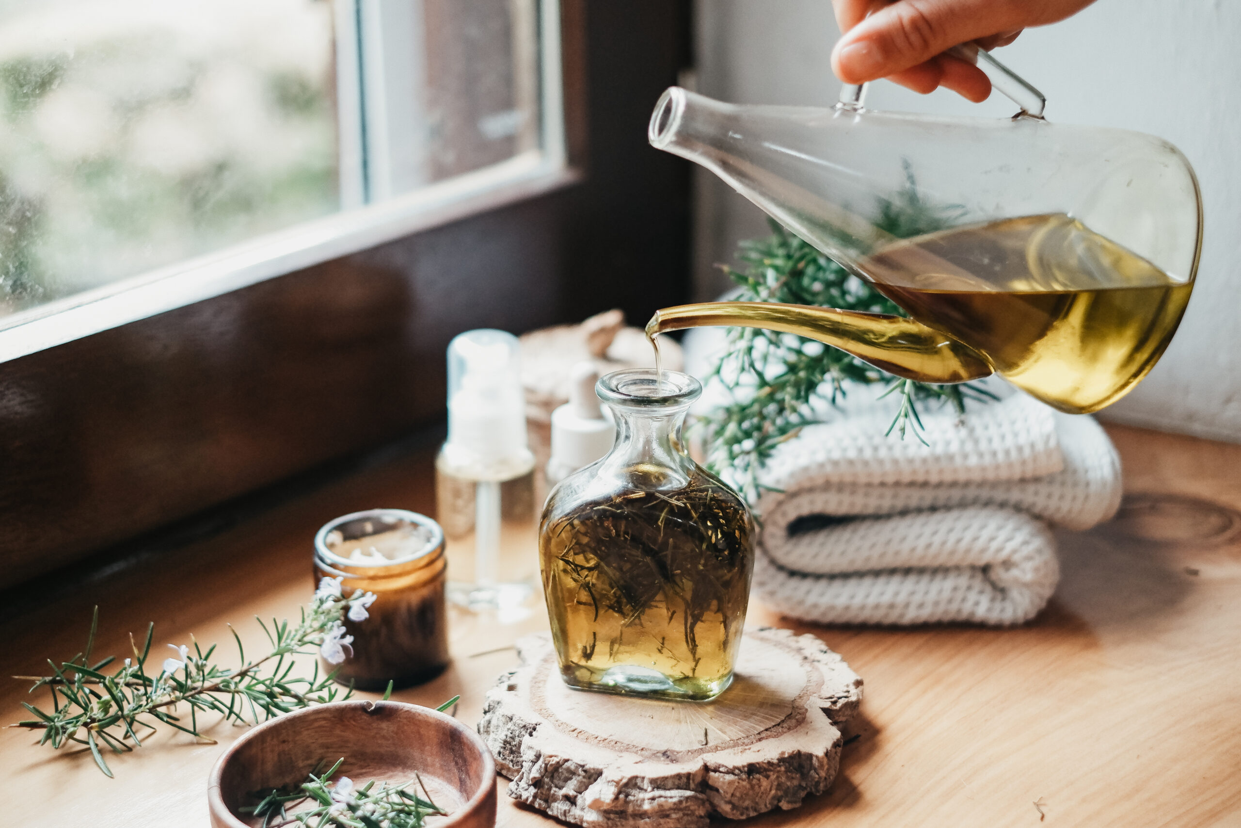 glass pitcher pouring oil into a jar of herbs