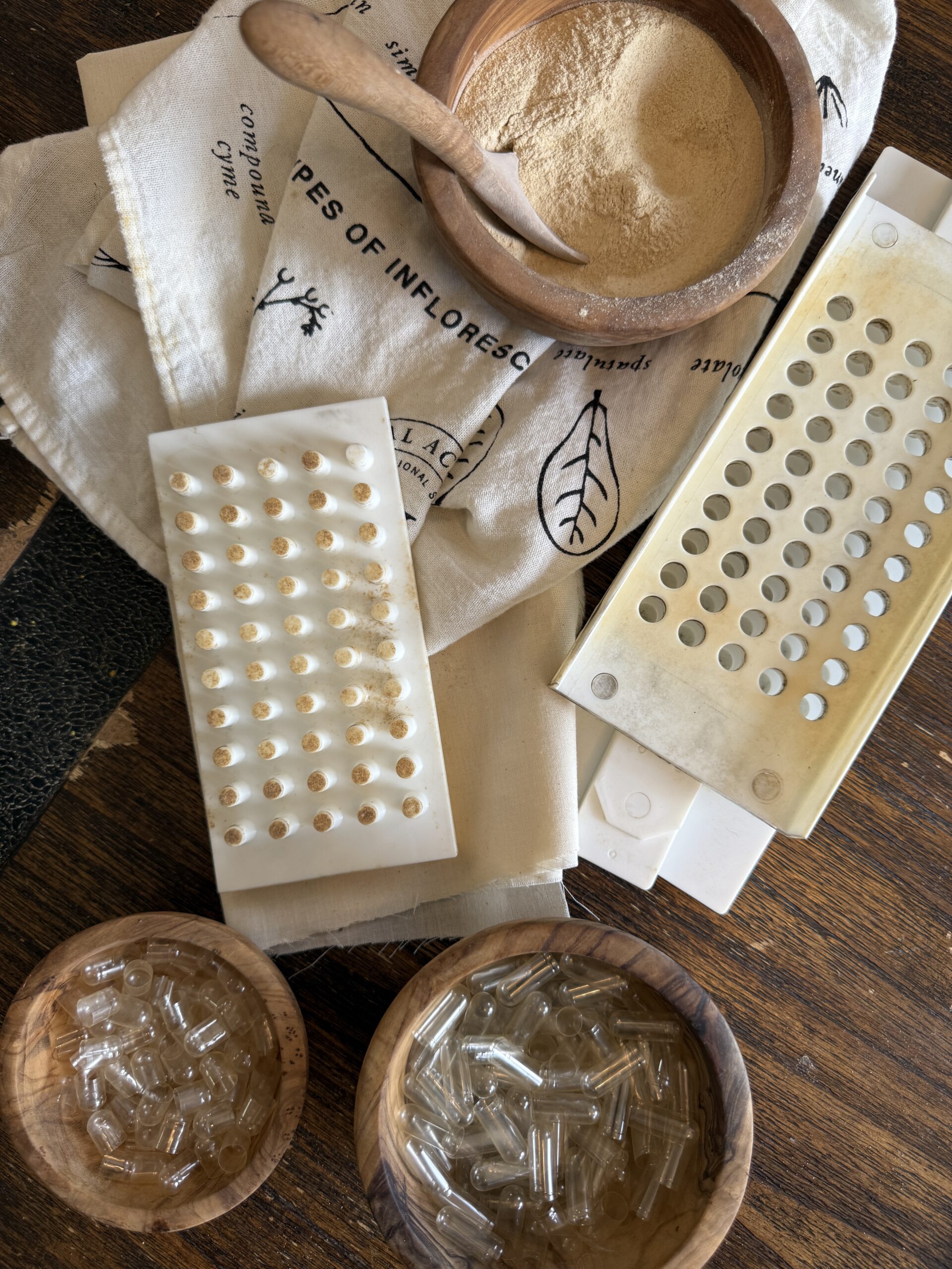 bowl of powdered herb, capsule machine, and bowls of empty capsules