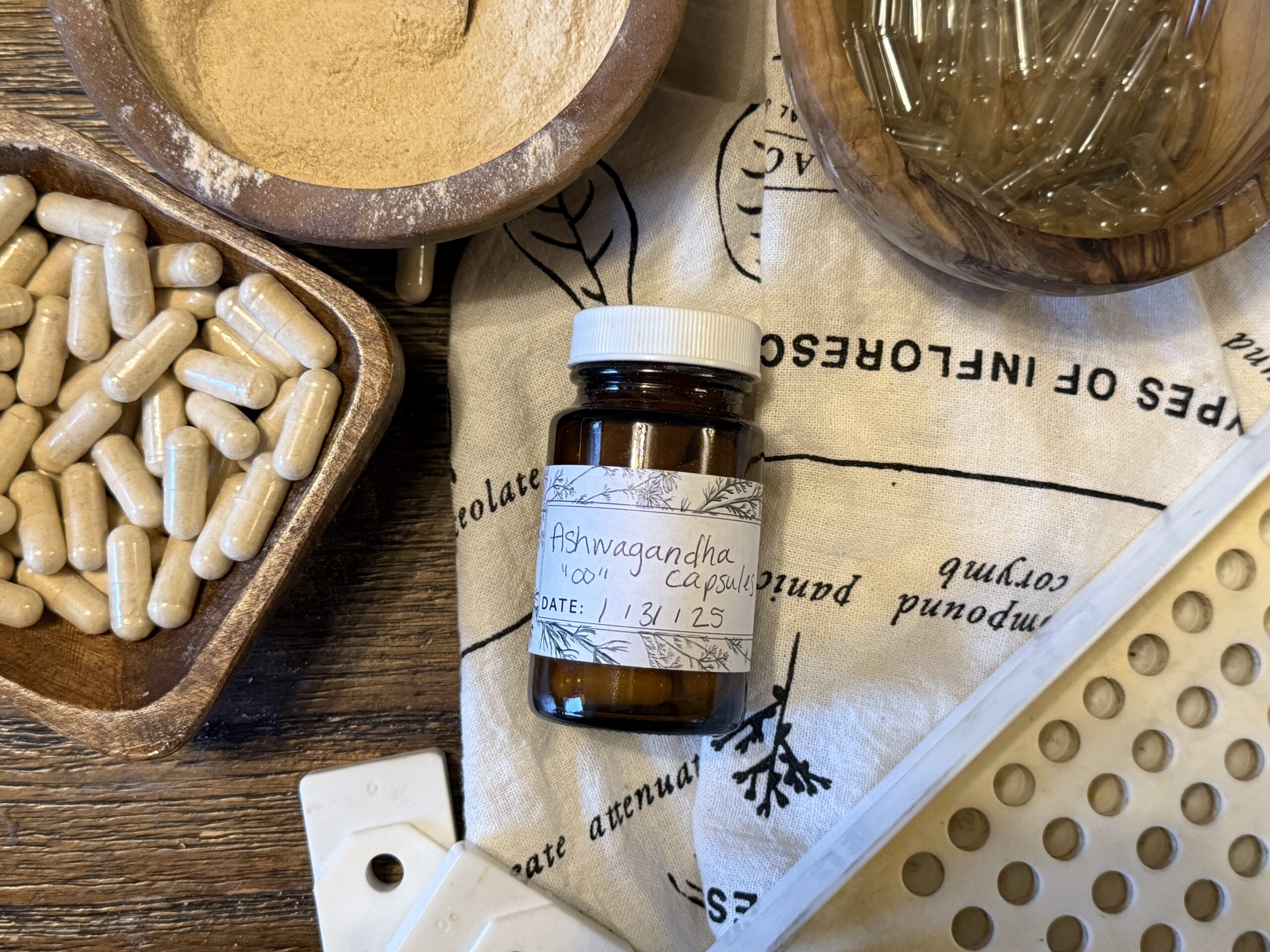 bottle of ashwagandha capsules with bowls of capsules, powdered herb, and empty capsules