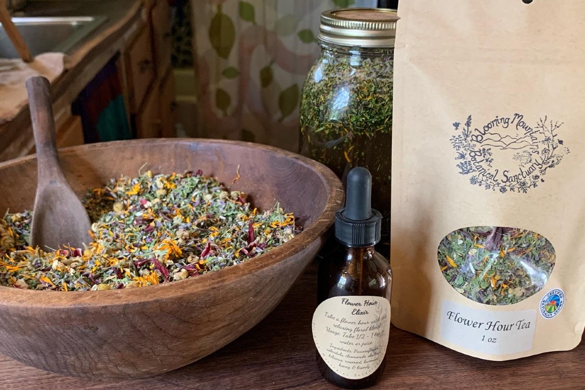 wooden bowl of herbs with a bottle of tincture and bag of herbal tea