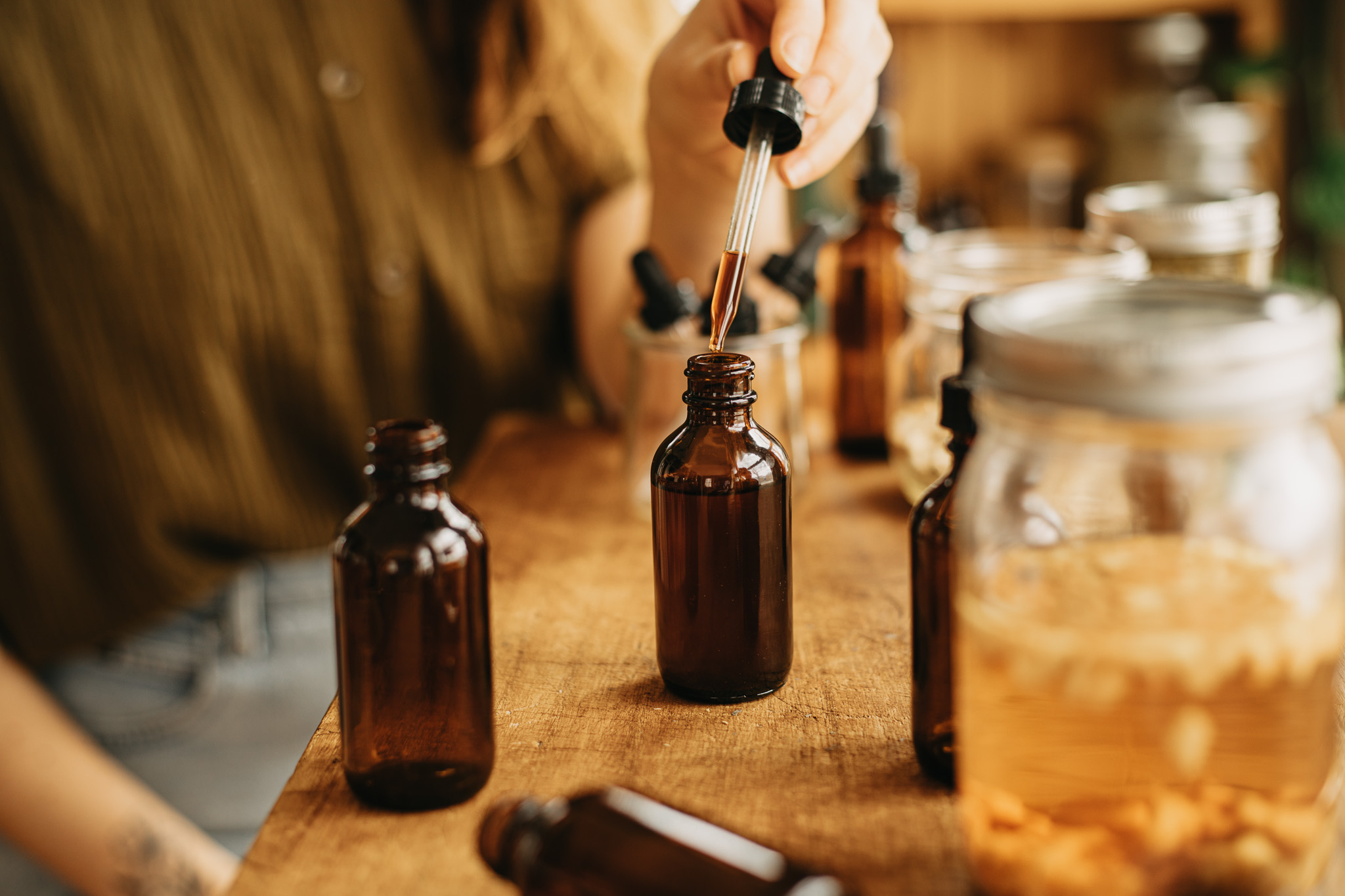 hand holding a dropper of herbal bitters with tincture bottles on a table