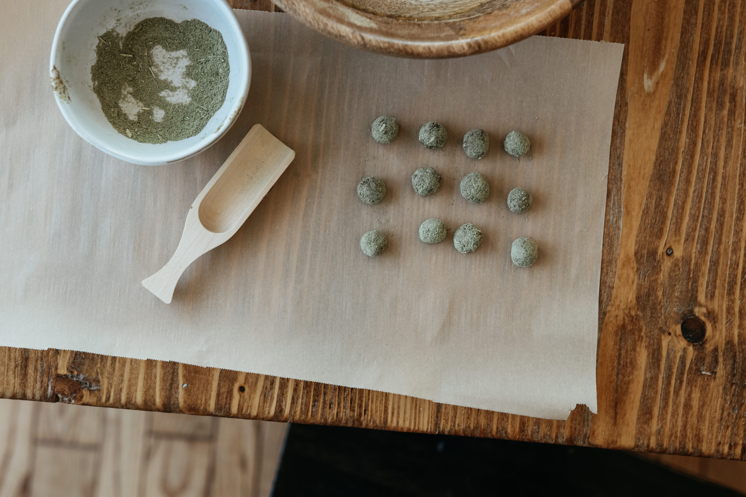 bowl of powdered herbs, wooden scoop, and balls of bitter pastilles on parchment paper