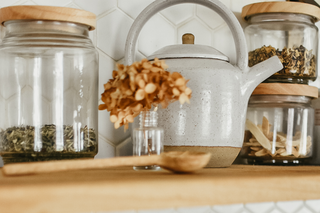 teapot surrounded by a vase of flowers and jars of herbs