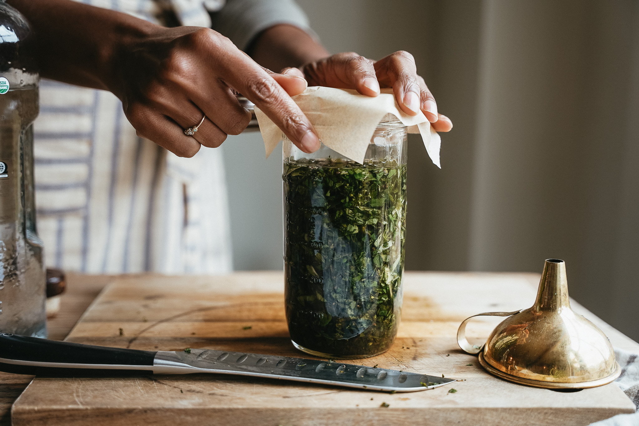 woman placing cheesecloth on a jar of herbs