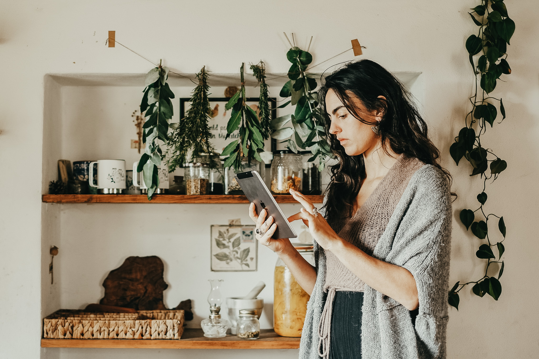 woman looking at iPad with herbs drying in front of shelves