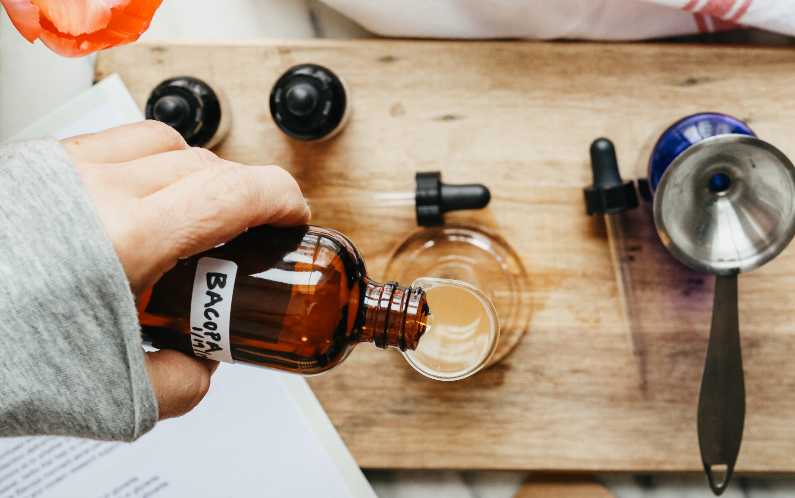 woman pouring a tincture into a glass with tinctures bottles next to it