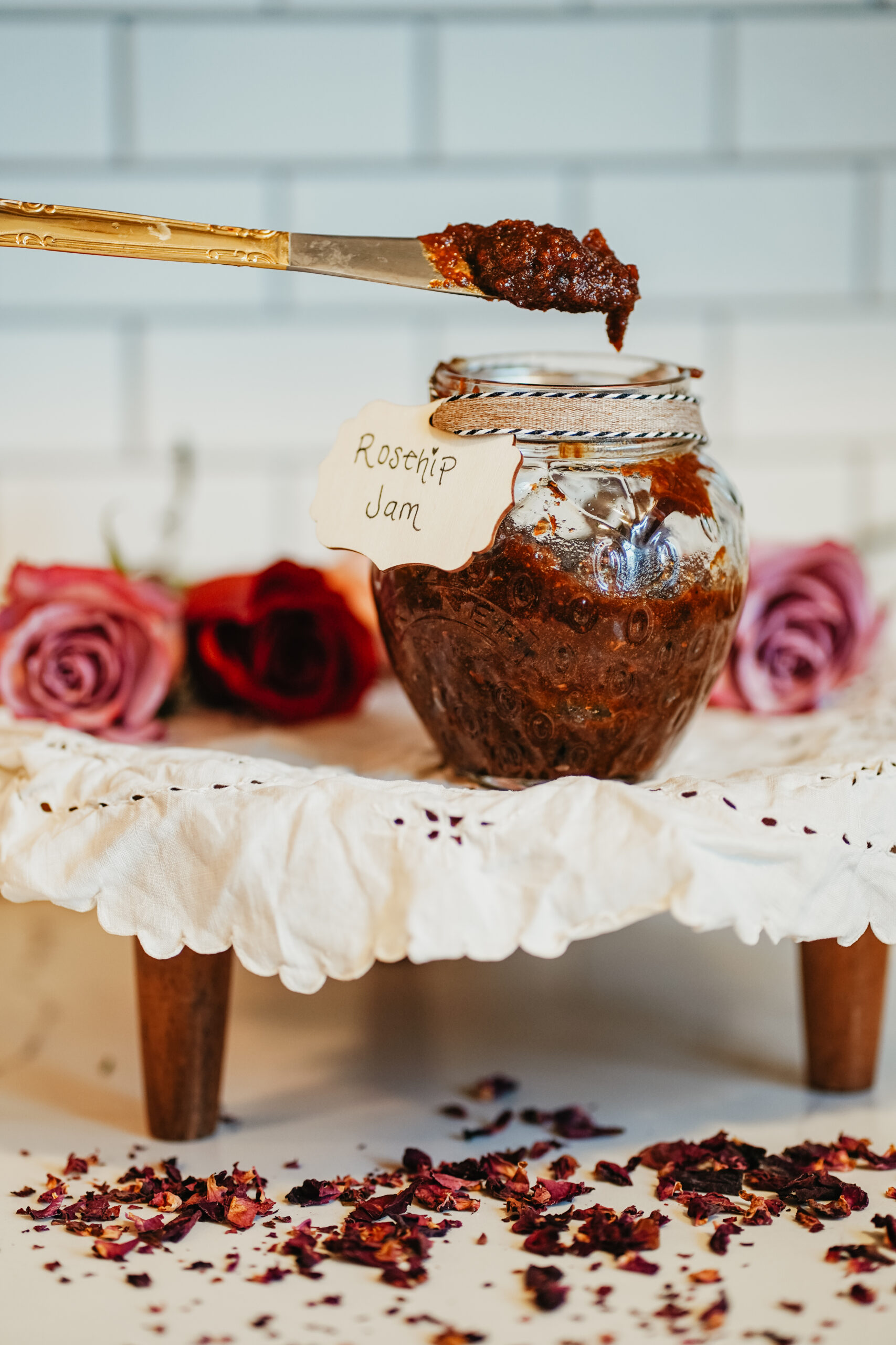 Discover this shimmering jam that perfectly captures the subtle beauty of the changing seasons: a Rosey Rose Hip Jam recipe. a jar of rose hip jam sitting on a small wooden riser