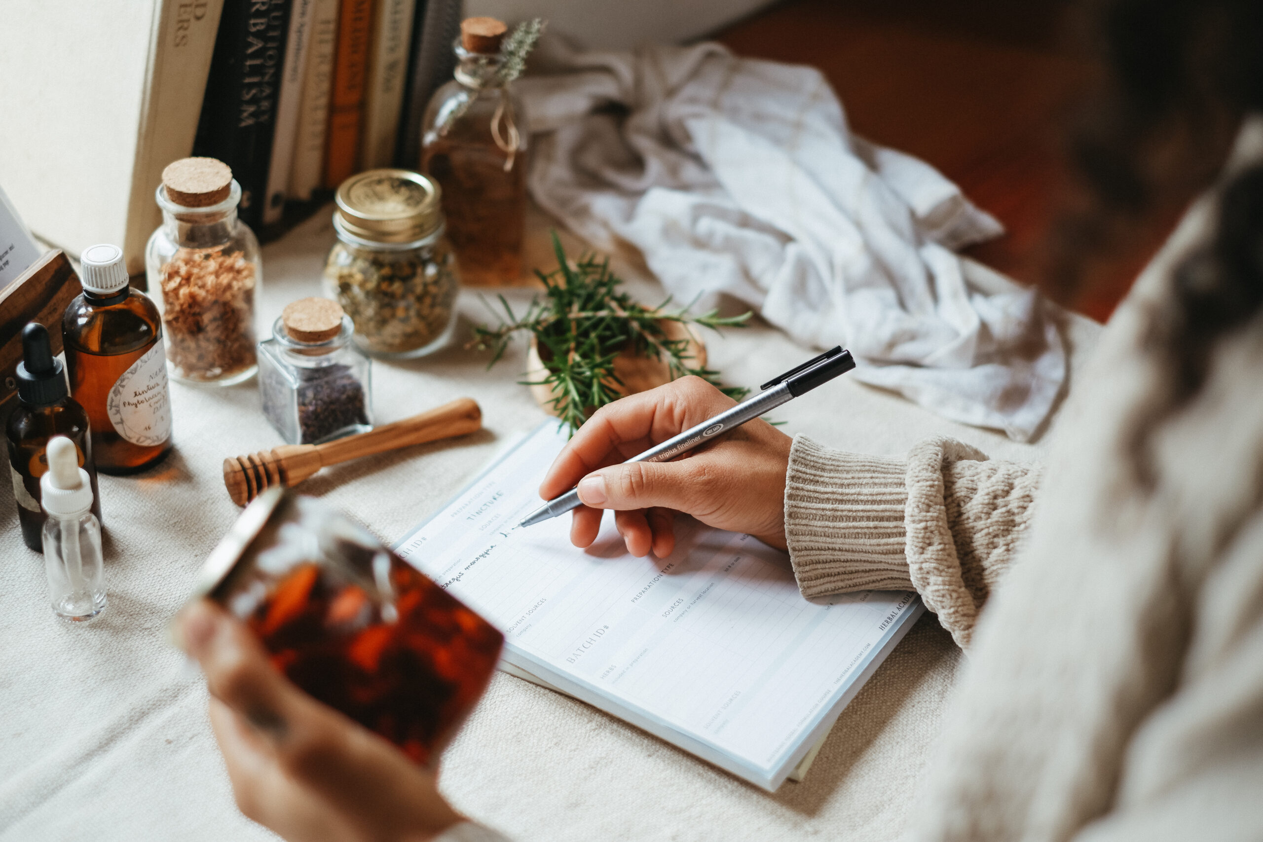 Person writing notes in notebook while holding an herbal preparation (1)