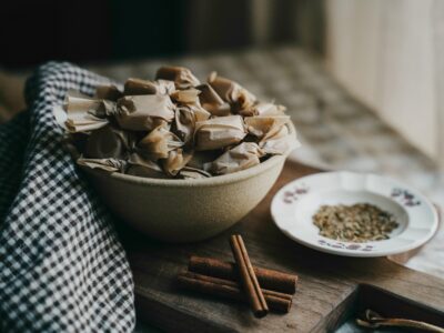 bowl of wrapped caramels with cumin and cinnamon sticks next to it on a table