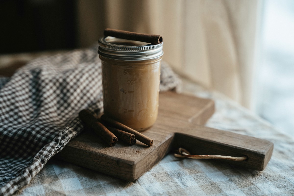 Spiced Caramels jar of caramel and cinnamon sticks on a wooden cutting board