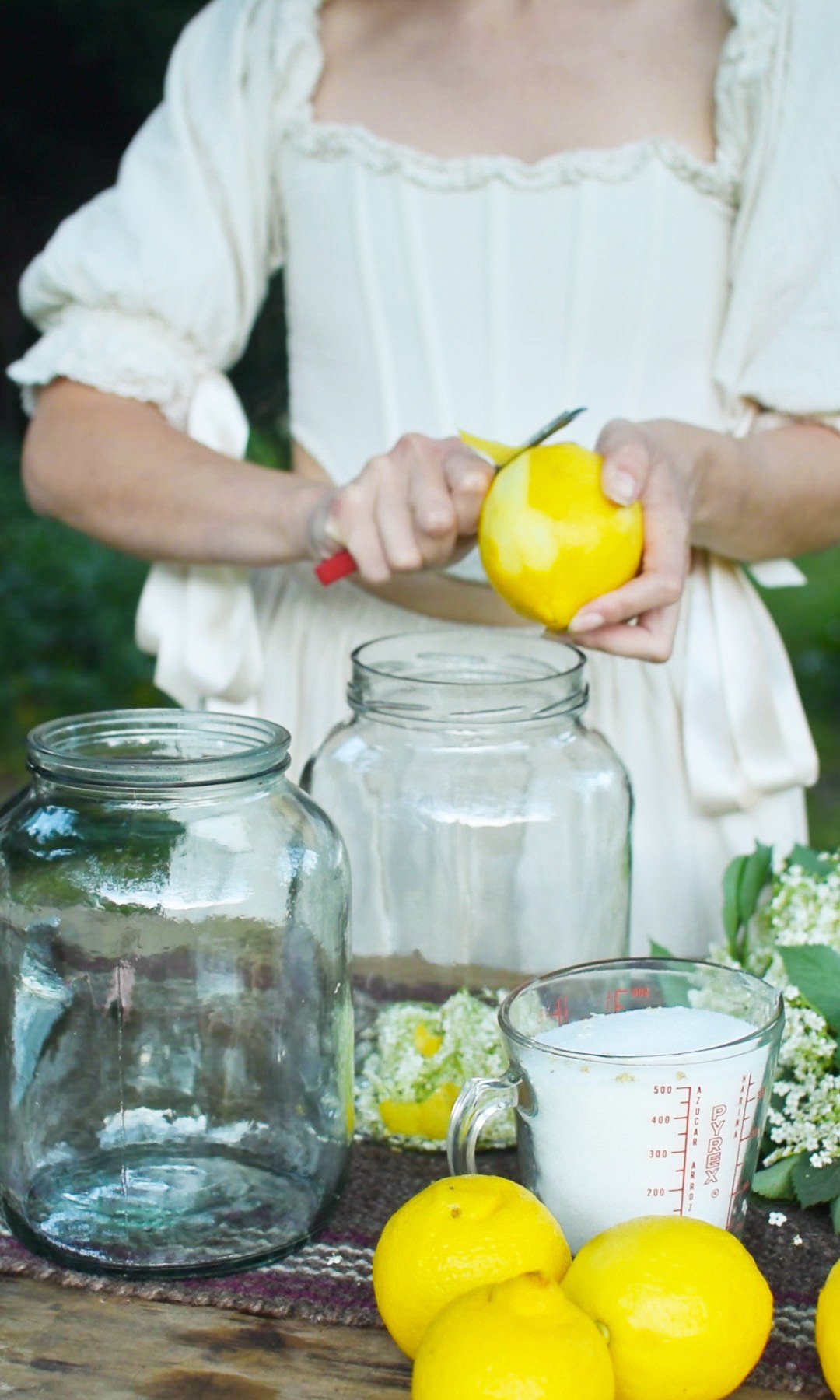 woman cutting lemon peel into a jar of elderflowers