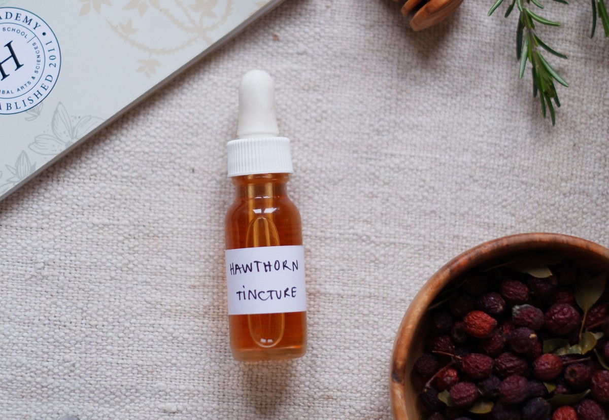 bottle of hawthorn tincture lying on a table with a bowl of hawthorn berries next to it