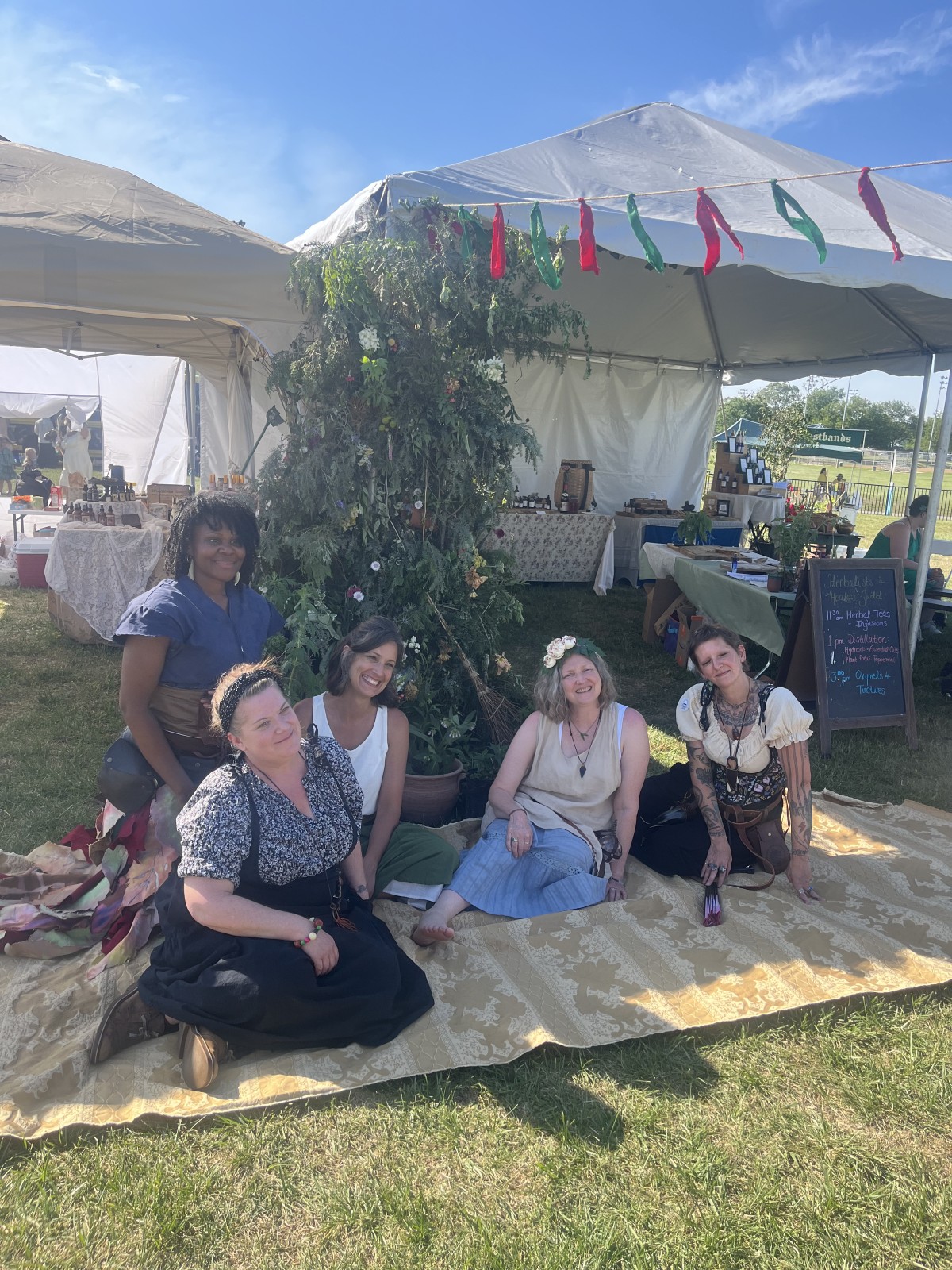 Rae sitting among friends on a large rug in front of a tent.