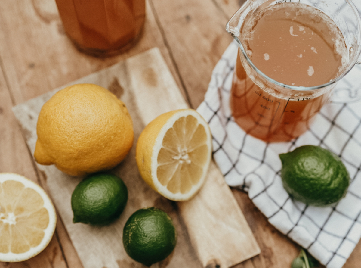 measuring cup with strawberry lemonade and lemons and limes on the table next to it