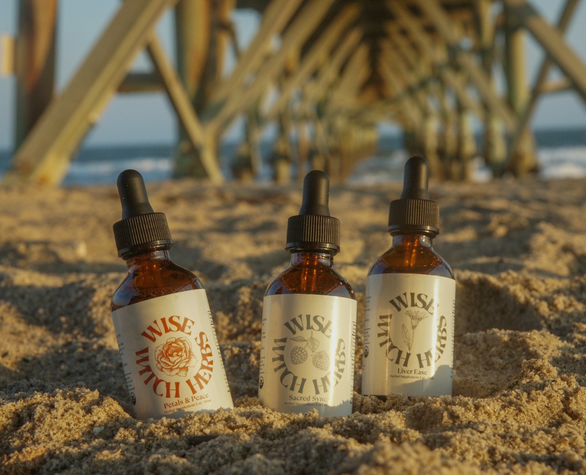 herbal products in the sand with the ocean and bridge in the background
