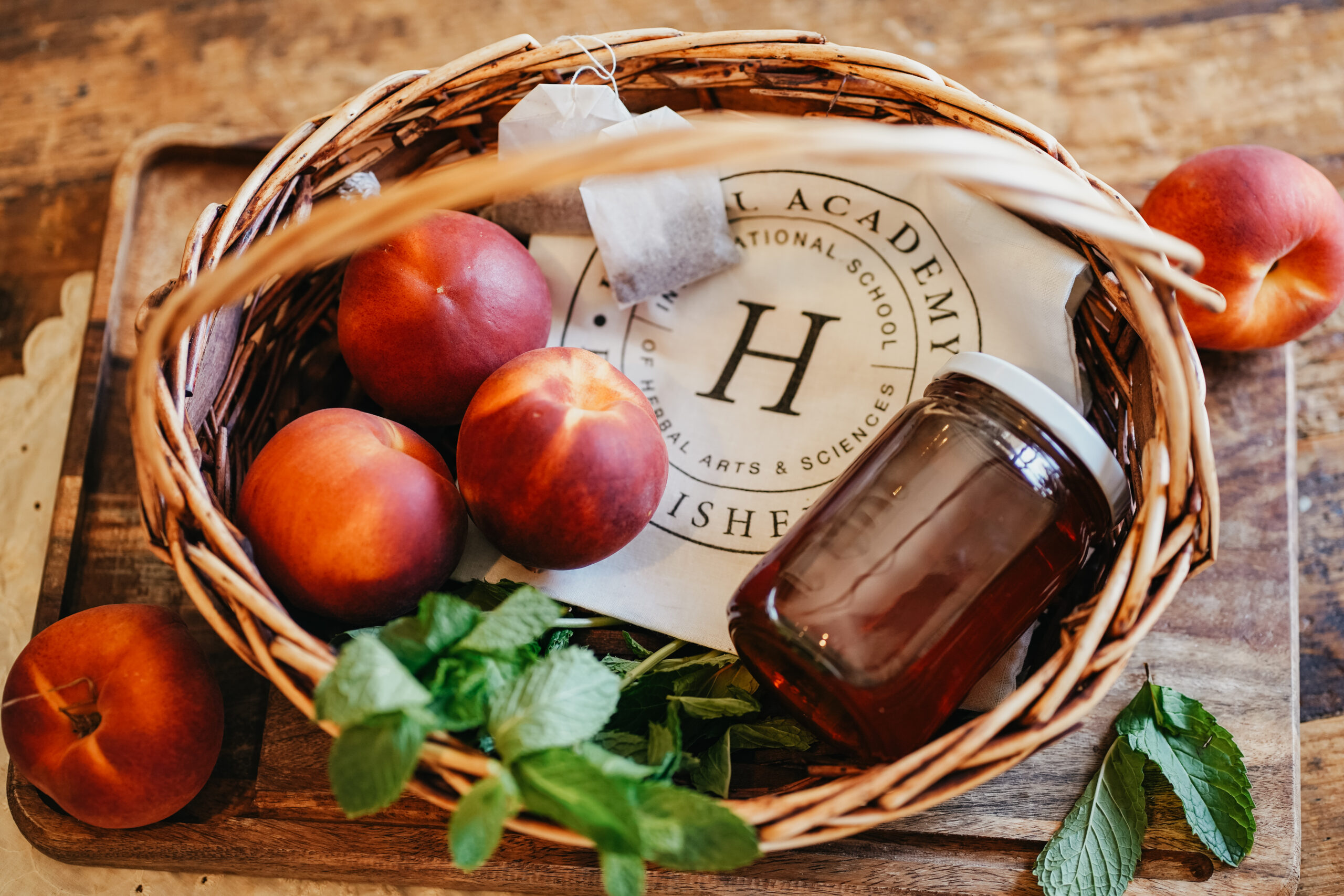 basket with peaches, a jar, and an Herbal Academy apron inside