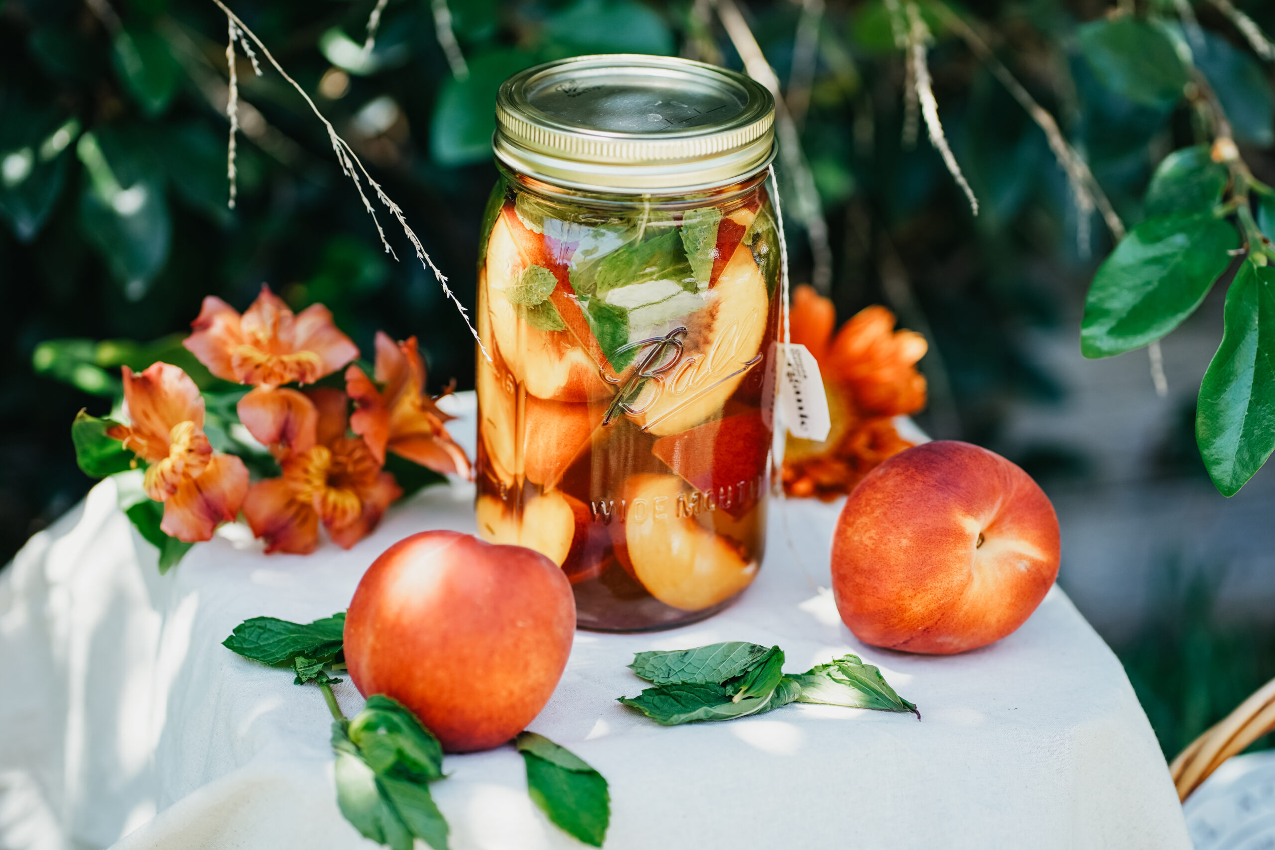 jar of peppy peach tea on a table with flowers and peaches on the table next to it