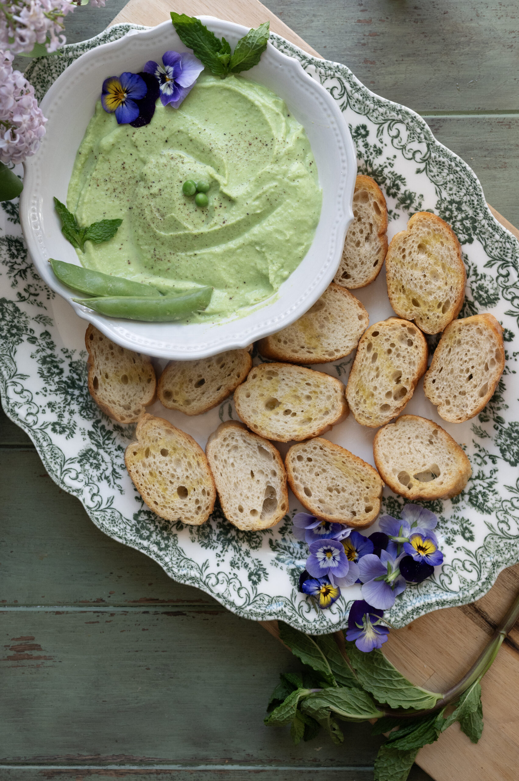 pea and mint crostini in a white bowl with bread slices on a platter