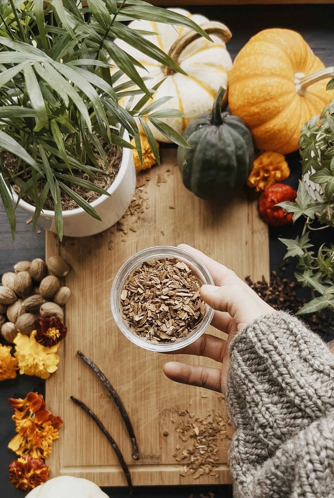 herbalist holding a jar of cinnamon over a wooden cutting board with ingredients in the background